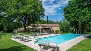 A rectangular swimming pool with lounge chairs and umbrellas, surrounded by a stone building and lush greenery. - Il Molinaccio 14+2, Emma Villas (Montepulciano (Siena))