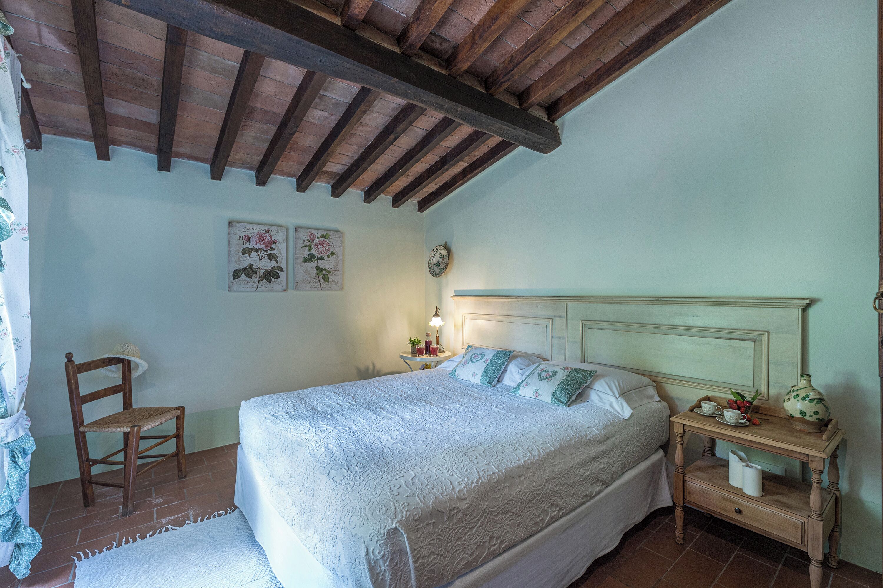 Ein Schlafzimmer mit einem Bett, einem Holzstuhl, einem Nachttisch und einer Wanduhr.