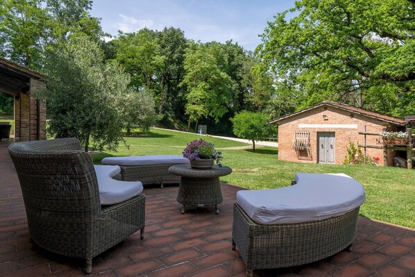 Une terrasse avec des meubles en osier, une petite table sur laquelle est posée une plante en pot, et un bâtiment en briques en arrière-plan.