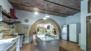 A spacious kitchen with a central island, stainless steel appliances, and a brick archway. - Il Molinaccio 14+2, Emma Villas (Montepulciano (Siena))