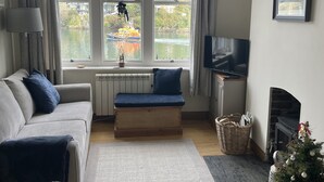 Un salon moderne avec un canapé, un banc, un téléviseur, une cheminée et une vue sur une rivière où naviguent des bateaux.