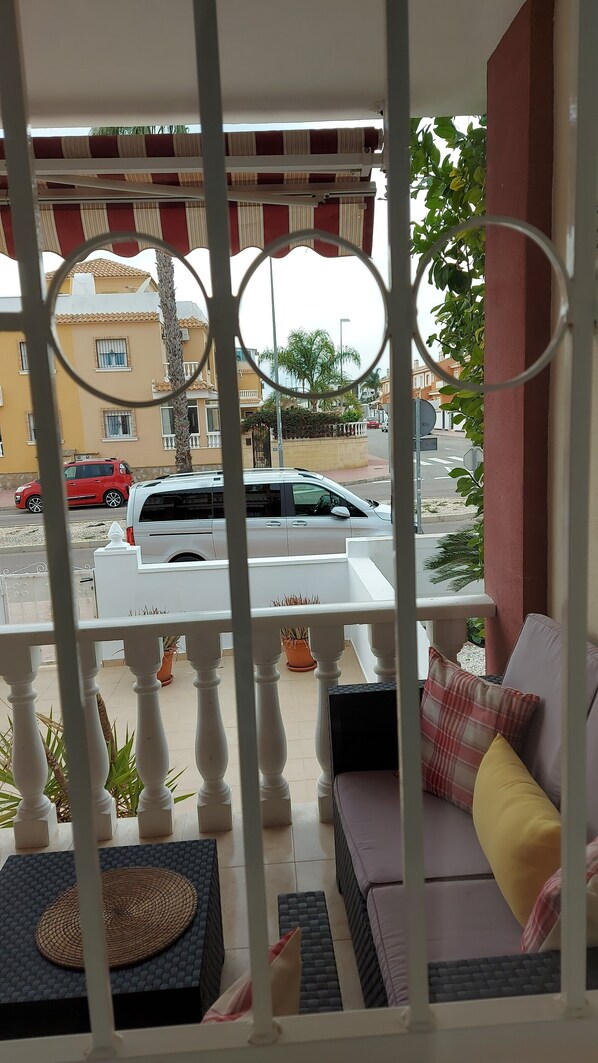 A balcony with a view of a street, a white car parked on the road, and a building with a yellow facade in the background. - Stunning Townhouse with Shared Communal Pool (Rojales)