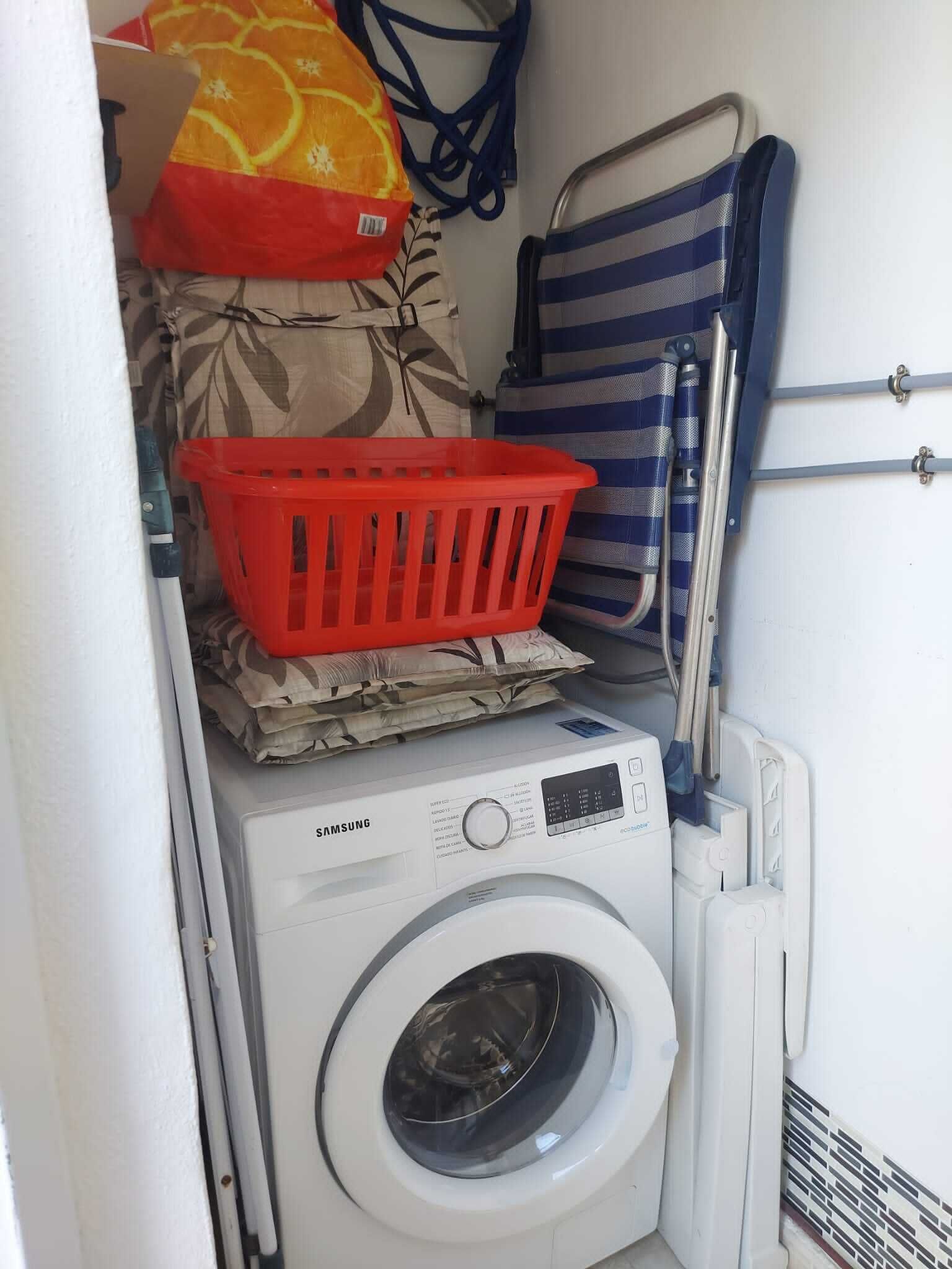 A compact laundry area with a Samsung washing machine, a red plastic basket, and a striped towel rack.