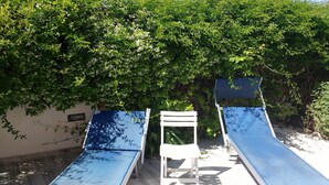 Dos tumbonas azules con sillas blancas, ubicadas bajo un denso dosel de follaje verde.