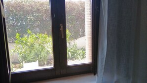 Una ventana con vista a un jardín y una cortina blanca parcialmente corrida.