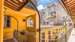Un edificio amarillo con balcón, baranda de metal y vista de edificios vecinos.