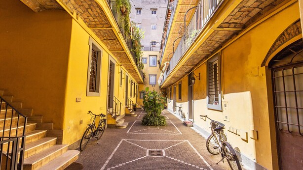 Un estrecho callejón con edificios amarillos, un camino empedrado en el centro y bicicletas aparcadas a los lados.