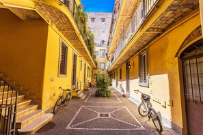 Une ruelle étroite bordée d’immeubles jaunes, avec un chemin central pavé et des vélos garés le long des murs.