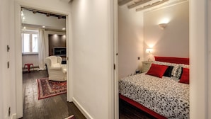Un dormitorio con cama, mesita de noche, silla y colcha estampada en rojo y blanco.