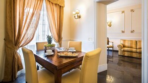 Uma sala de jantar com uma mesa de madeira, cadeiras, uma fruteira e uma xícara de café. Há um sofá e um espelho ao fundo.