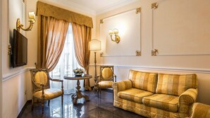 Um quarto luxuoso com sofá estampado em dourado, cadeiras ornamentadas, uma pequena mesa com um vaso e um espelho grande na parede.