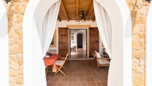 Een interieur van een kamer met stenen muren, een betegelde vloer, een houten plafond en een tafel met stoelen.