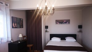 Ein Schlafzimmer mit Bett, Schminktisch, Stuhl, einer Chandelierleuchtre und Kunstwerken an den Wänden.