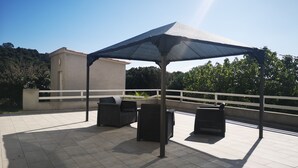 Eine Terrasse im Freien mit überdachter Sitzecke, einem Mülleimer und einem Gebäude im Hintergrund.