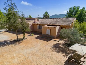 Un edificio a due piani con tetto in tegole, una piccola zona giardino con una panchina e un cortile lastricato.