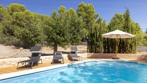 Una piscina con sillas de descanso y una sombrilla, rodeada de árboles.