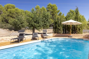 Una piscina con lettini e un ombrellone, immersa nel verde.