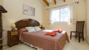 Un dormitorio con cama, mesita de noche, silla, ventana con cortinas y aire acondicionado instalado en la pared.