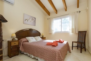 Una camera da letto con un letto, un comodino, una sedia, una finestra con tende e un condizionatore d'aria a parete.