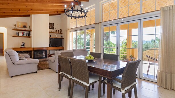 Un salón amplio con chimenea, un comedor con sillas de mimbre y ventanas grandes que ofrecen vistas al exterior.