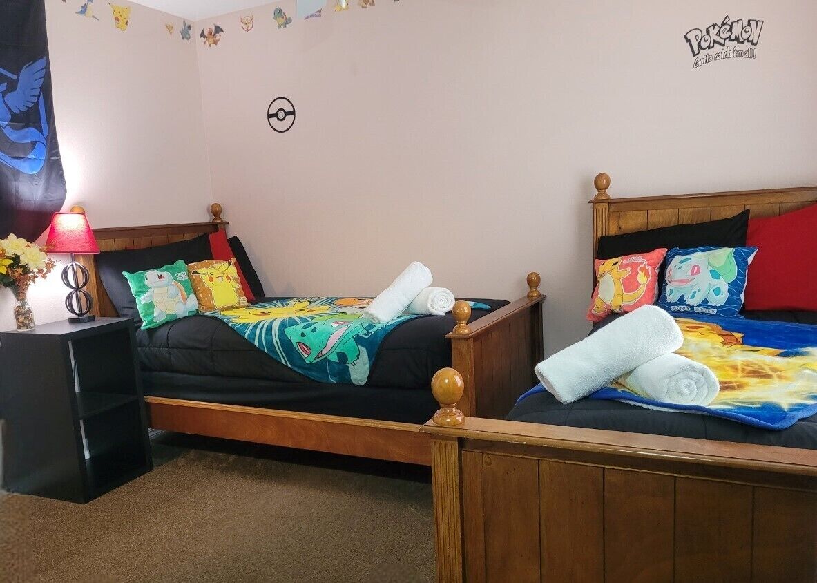 A bedroom with two wooden beds, each with colorful bedding and pillows. There is a nightstand with a lamp and a vase of flowers.