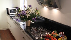 Una cocina moderna con estufa de acero inoxidable, microondas y un fregadero. Hay un florero con flores en la encimera.
