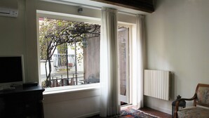 Una habitación con un ventanal grande, una alfombra estampada, una silla y un radiador.