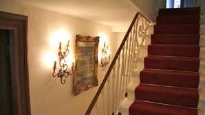 Una escalera con peldaños alfombrados de rojo y barandillas blancas, que conduce a un piso superior.
