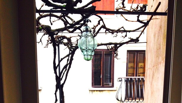Un espacio exterior reducido con una mesa, sillas, un farol y una planta en maceta.