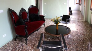 A room with a red sofa, a black chair, a round table with a vase, and a chandelier. - In the heart of Venice (Venise)