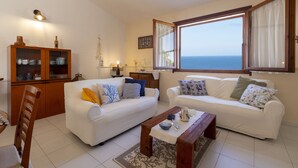Una sala de estar con dos sofás blancos, un mueble de madera y vista al mar.