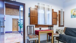 A living room with a wooden table, two chairs, a sofa, and a window with wooden shutters.