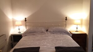 A neatly made bed with a metal frame, two bedside tables with lamps, and a wall-mounted switch.
