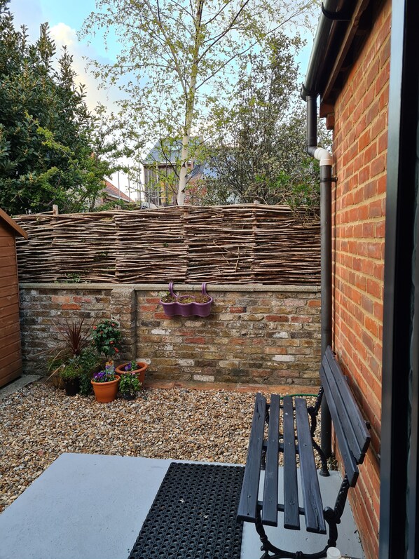 A patio area with a bench, potted plants, and a brick wall.
