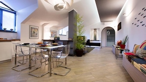 Een moderne keuken met een eethoek, met een centraal kookeiland, transparante stoelen en een grote potplant.