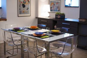 Un'area pranzo moderna con un tavolo bianco, sedie trasparenti e piatti colorati.