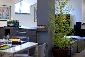 Une cuisine moderne avec une table à manger, des chaises, une plante en pot et des œuvres d’art accrochées aux murs.