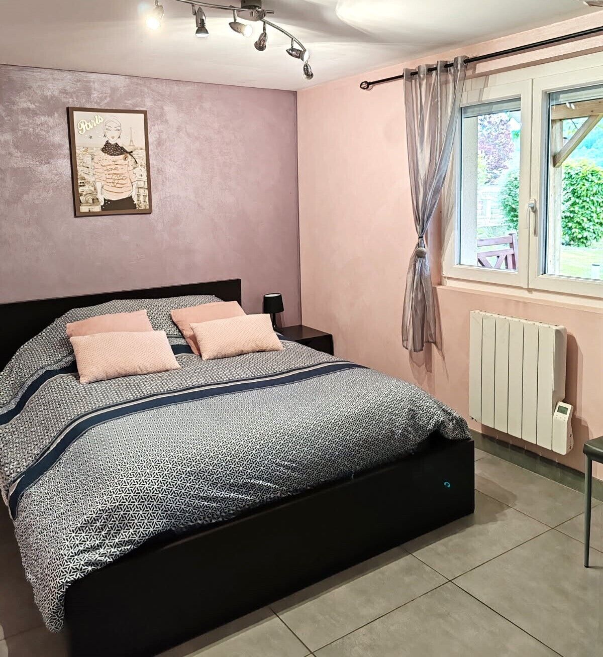A bedroom with a bed, a bedside table, a lamp, a radiator, and a window with curtains.