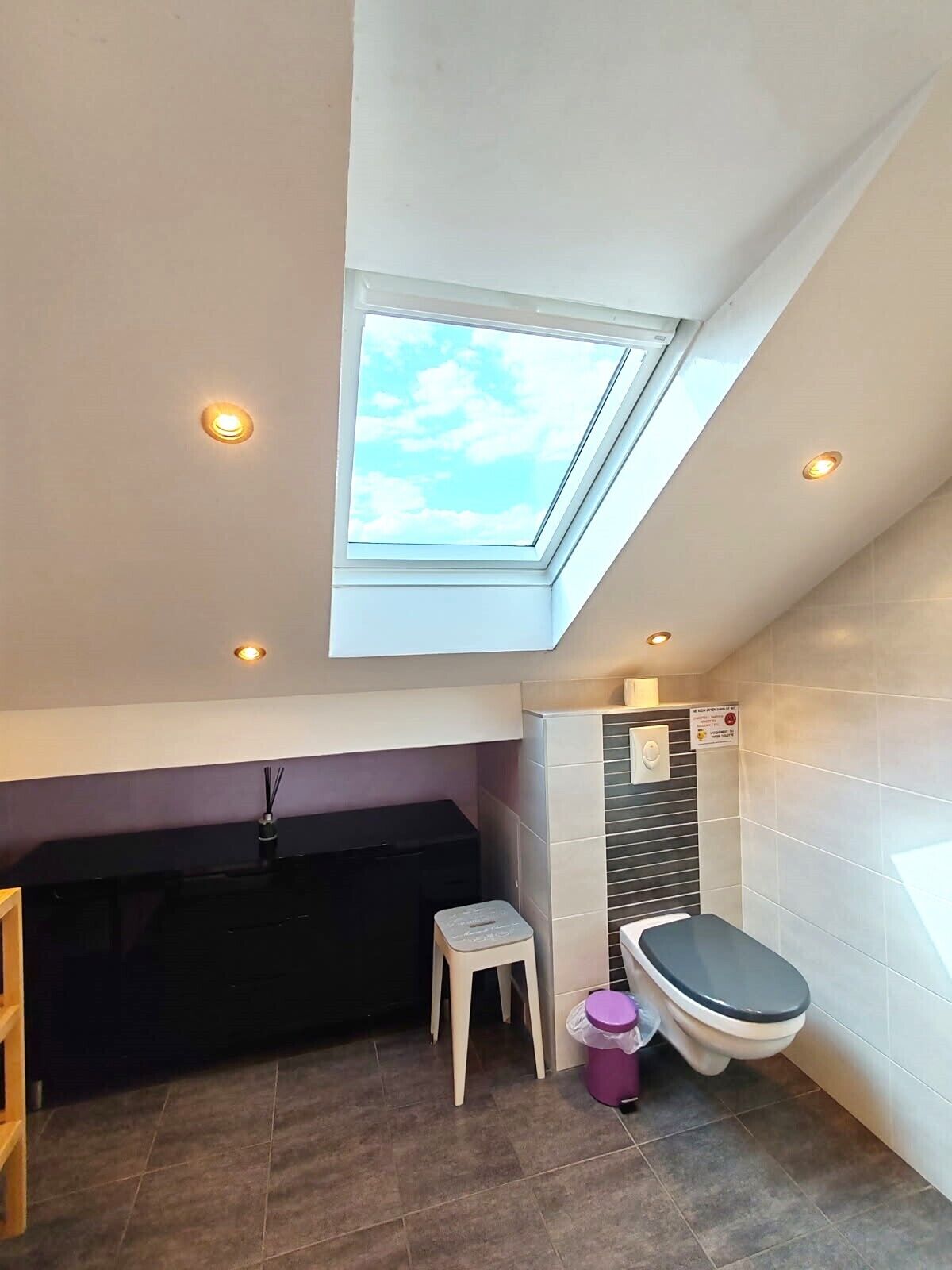 A compact bathroom with a skylight, a bathtub, a toilet, and a small stool.