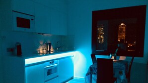 Une cuisine moderne dotée d’un four encastré, un coin repas avec une table et des chaises, et une vue sur les bâtiments de la ville la nuit.