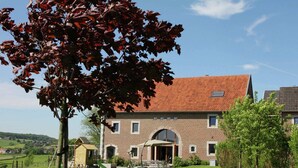 A two-story brick house with a red-tiled roof, a front porch, and a small play area with a slide. - Holiday home in Limbourg with garden (Limbourg)