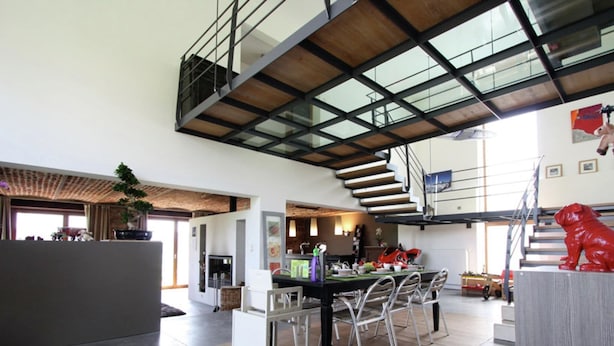 A spacious living area with a high ceiling, a dining table, chairs, a staircase, and a red sculpture. - Holiday home in Limbourg with garden (Limbourg)