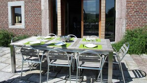 An outdoor dining area with a brick building, a large arched doorway, and a table set for four with metal chairs. - Holiday home in Limbourg with garden (Limbourg)