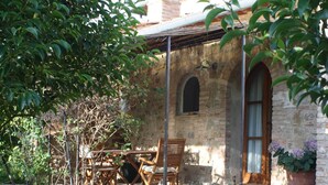 Eine Terrasse im Freien mit Tisch und Stühlen, ein Steinhaus mit Rundbogenfenstern und ein Topfpflanzen.