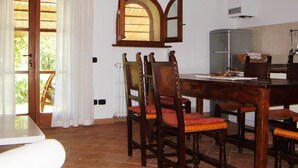Ein Essbereich mit Holztisch und Stühlen, einem Fenster mit Vorhängen und einer Küchenzeile mit Kühlschrank.