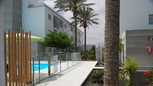 A modern building with a swimming pool, palm trees, and a glass railing. - PRETTY APARTMENT WITH POOL AT BRISTOL SUNSET  (Corralejo)