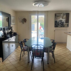 A dining area with a glass-top table and chairs, a kitchen with cabinets, and a view through a glass door. - La Salvetat Saint Gilles: House / Villa - LA SALVETAT ST GILLES (La Salvetat-Saint-Gilles)