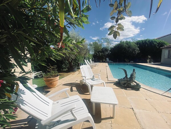 Piscina com cadeiras de sol brancas e um pátio de pedra.