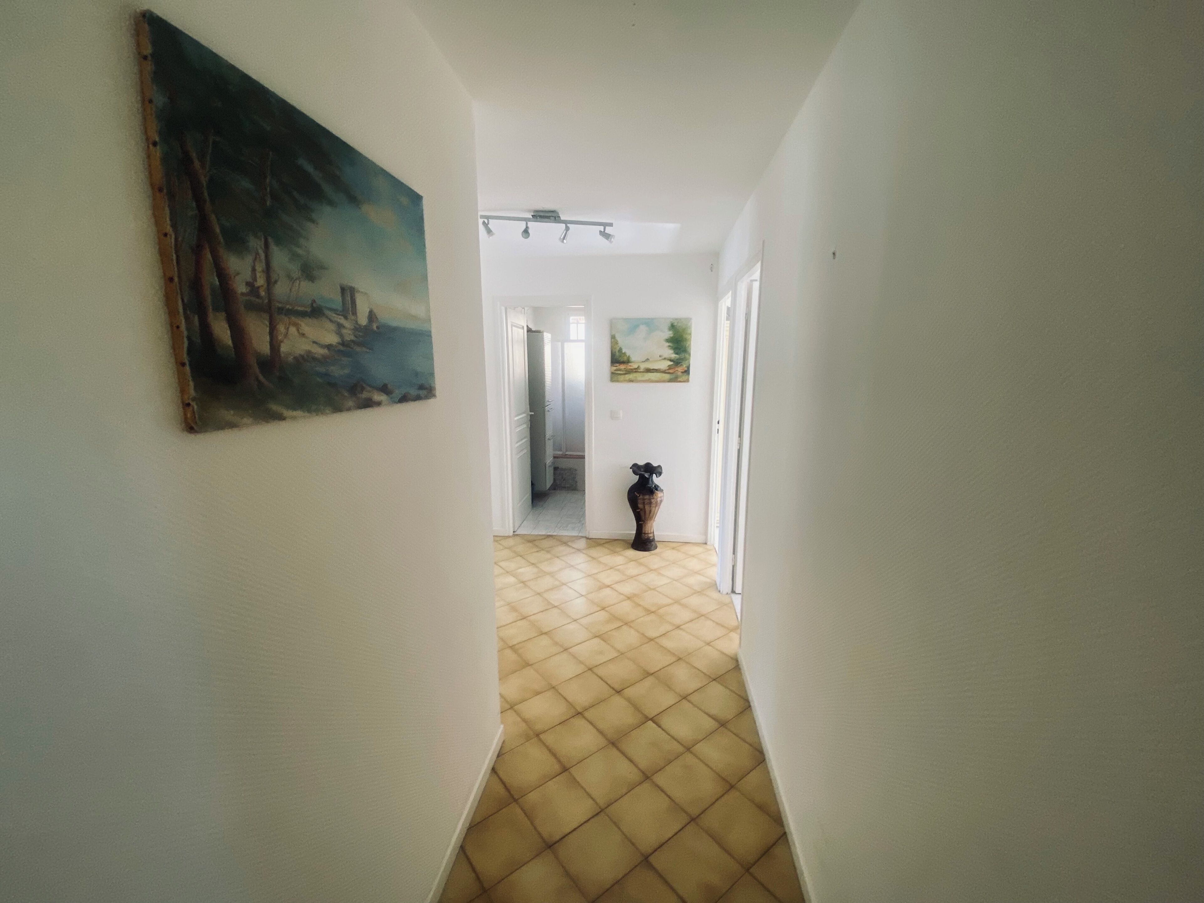Ein Flur mit Fliesenboden, einem Gemälde an der linken Wand und einer Tür am Ende, die in einen anderen Raum führt.