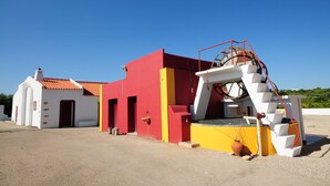 Un edificio con fachada roja y blanca, una gran rueda hidráulica y una escalera que conduce a un nivel superior.
